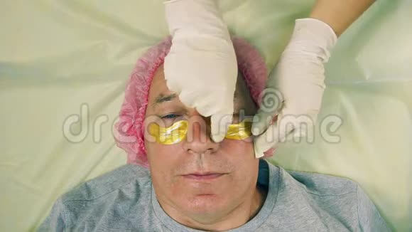 一个戴着手套的美容师的手从男人的眼睛下面的胶原蛋白垫上移开视频的预览图