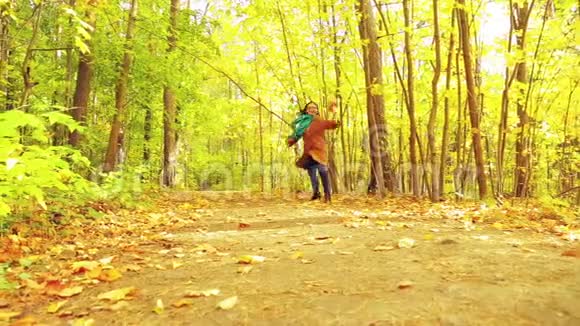 在一个秋天的公园里一个穿着外套和围巾的年轻黑发女人手里拿着枫叶沿着一条小路跑视频的预览图