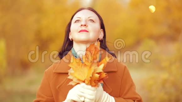 秋天公园里的一位年轻女子手里拿着一束枫叶在欣赏大自然慢动作视频的预览图