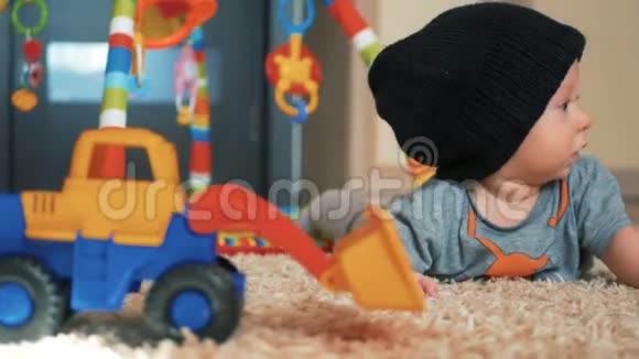 可爱的小男孩戴着帽子玩具躺在家里的地板上视频的预览图