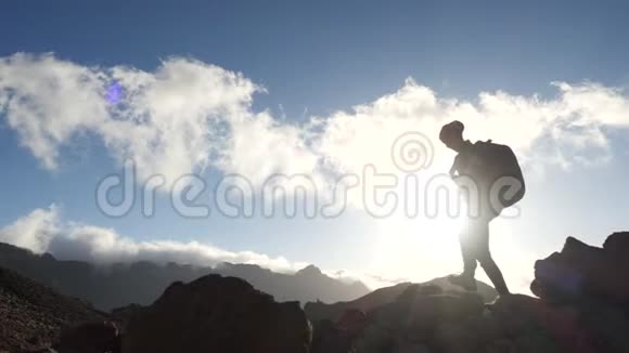 一个年轻女子徒步旅行的剪影背着背包在蓝天和云彩的映衬下朝山顶走去慢动作视频的预览图