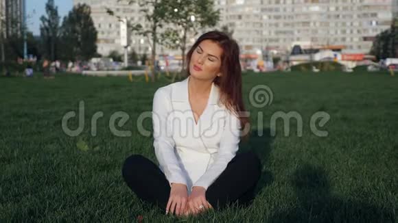 穿着白色西装坐在户外冥想的年轻女商人视频的预览图