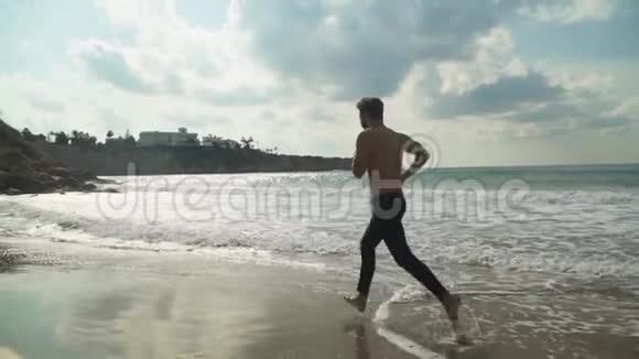 阳光明媚的一天在风景如画的美丽海滩上半裸的运动男子在户外跑步慢动作视频的预览图