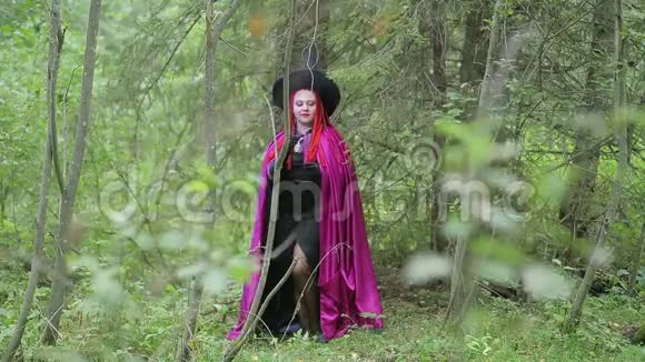 年轻的女巫红发黑帽子覆盆子斗篷在森林里点燃蜡烛视频的预览图