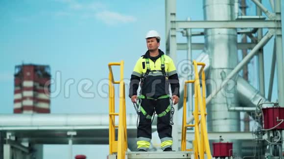自信的男性金属工人站在塔上看着大工厂的领土视频的预览图