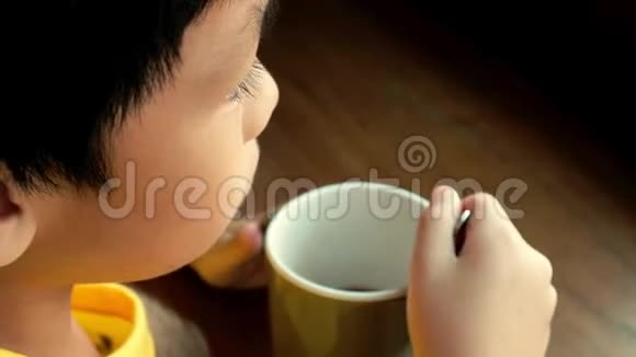 一个小男孩坐在家窗边的木桌旁喝一杯热巧克力他左手拿着杯子视频的预览图