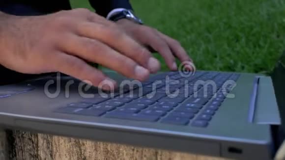 商人用手提电脑键盘打字的特写镜头在公园里用笔记本电脑的人网络通信的概念自由职业的视频的预览图