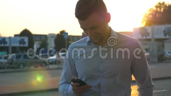 年轻的成功商人穿着衬衫站在城市环境中日落时使用智能手机帅哥视频的预览图