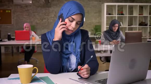 令人敬畏的阿拉伯女孩专注于电话交谈而坐在电脑后的桌面上视频的预览图