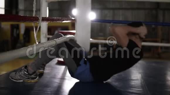 拳击手坐在拳击场的地板上训练腹部肌肉把躯干抬到拳击绳上培训视频的预览图
