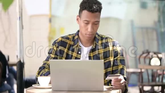 非洲青年男子在笔记本电脑上在线购物室外咖啡厅视频的预览图