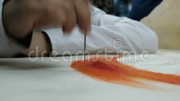 一个穿白色衬衫的孩子用橙色干毡工作在白色织物底座上填充一种彩色羊毛图案视频的预览图