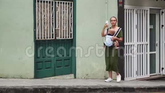 妈妈带着一个婴儿在一条狭窄的老街上散步并为社交网络拍摄了一段关于她在旅途中的视频视频的预览图