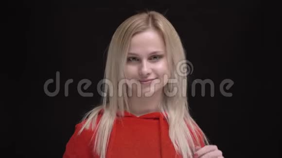 年轻的白发白种人女孩穿着红色毛衣的肖像在黑色背景上调情地把头发摇成相机视频的预览图