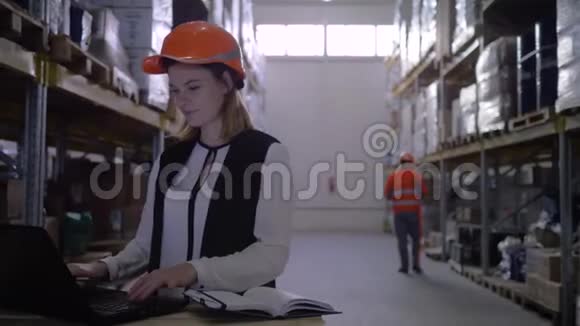 戴着安全帽的女工在仓库里用笔记本电脑做笔记视频的预览图