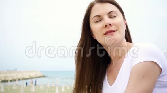 年轻女子坐在海滩上的肖像从地中海吹来的风慢慢地吹着她的头发视频的预览图