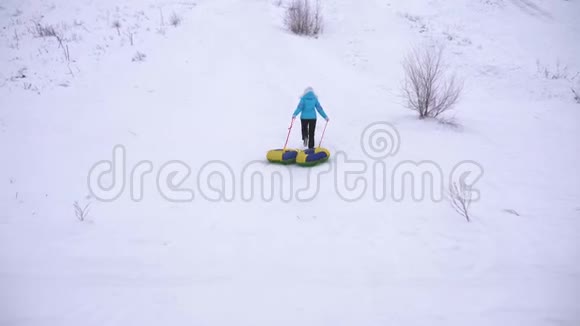 女孩跑在雪山上拉雪橇和一个充气雪管在冬季公园休息过圣诞假期视频的预览图