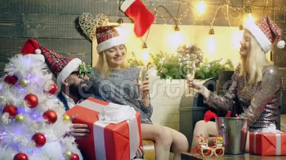 两个迷人的女孩和一个留胡子的男人庆祝圣诞节女孩和留胡子的男人在新的背景下喝香槟视频的预览图