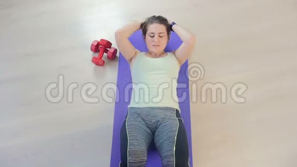 在客厅的健身垫上躺着绑腿的年轻女性做腹肌练习的视频视频的预览图