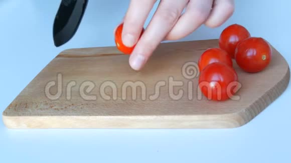 女人的手在白色的桌子背景和木制的厨房板上的树枝上切着美丽多汁成熟的红樱视频的预览图