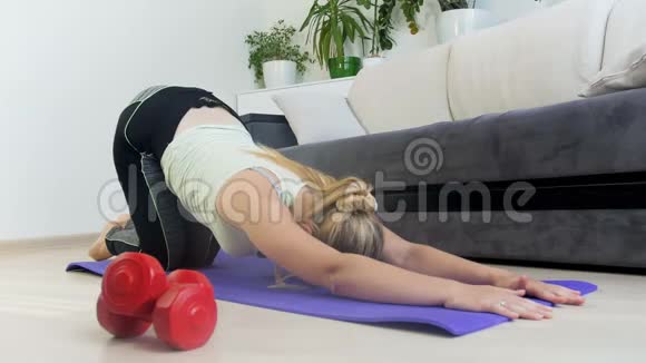年轻女子在家做健身运动后在瑜伽垫上伸展身体的4k镜头视频的预览图