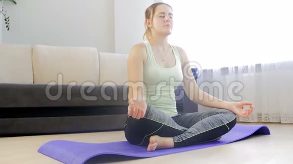 多莉4k镜头美丽的年轻女子坐在客厅的健身垫上莲花瑜伽姿势和冥想视频的预览图