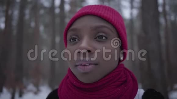 美国黑人女孩戴着红帽子戴着红领巾站在冬天的森林里正对着镜头观看视频的预览图