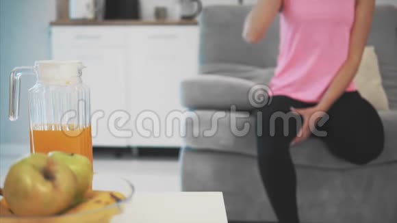 这个女孩是一种健康的生活方式从锻炼中获得巨大的乐趣坐在沙发上享受橙汁视频的预览图
