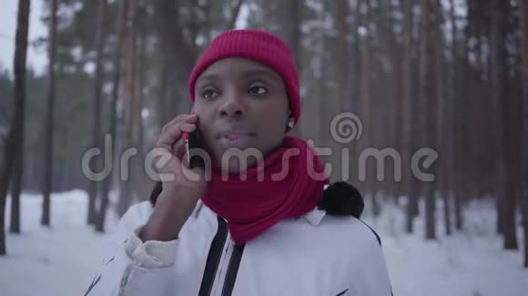 美国黑人女孩在冬天森林里用手机笑着近距离交谈的肖像穿暖和夹克的漂亮女孩视频的预览图