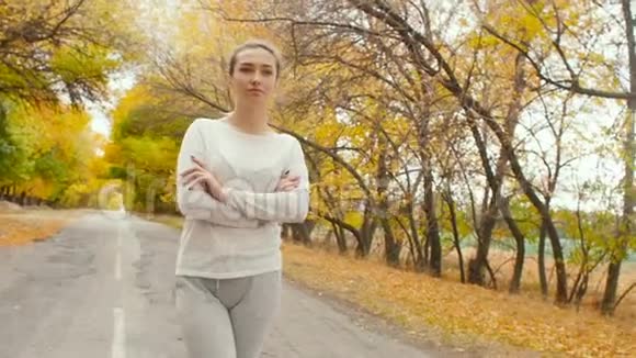 美丽的女孩穿着运动服装从事户外运动女人走在柏油路上开始沿着秋天的自然奔跑视频的预览图