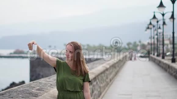 一个穿着绿色衣服的漂亮女孩在海边的一个手机上为博客拍摄视频视频的预览图