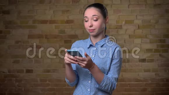 白种人妇女的肖像马尾辫观看智能手机与积极的笑声在布里克肯墙背景视频的预览图