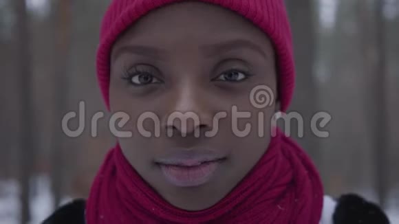 一位身穿红帽子和红领巾的美国黑人女孩站在一片白雪皑皑的森林中的特写视频的预览图