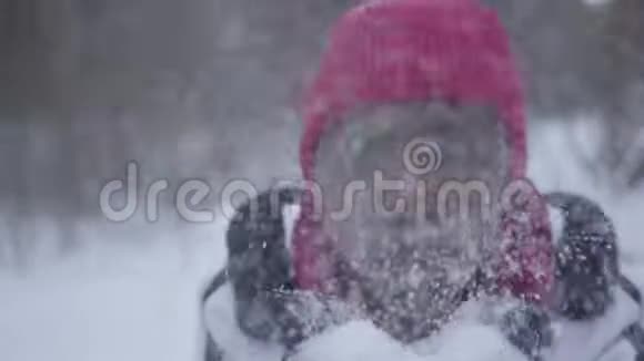 非洲裔美国年轻女性穿着温暖的衣服戴着豆帽和白色夹克从手中吹起雪花视频的预览图