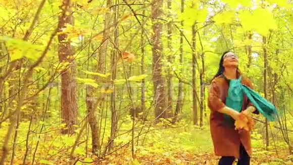 秋天公园里一个阳光明媚的日子里一个年轻开朗的女人手里拿着枫叶手里旋转着把树叶扔在里面视频的预览图