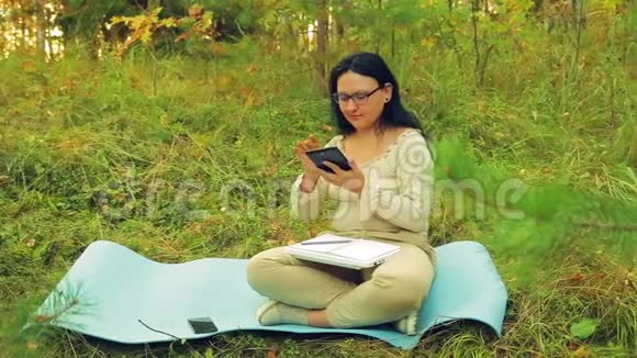 一位戴眼镜的妇女在森林边缘的平板电脑上工作上面有图表视频的预览图
