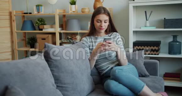 美丽的年轻女子在家中的沙发上触摸智能手机屏幕视频的预览图