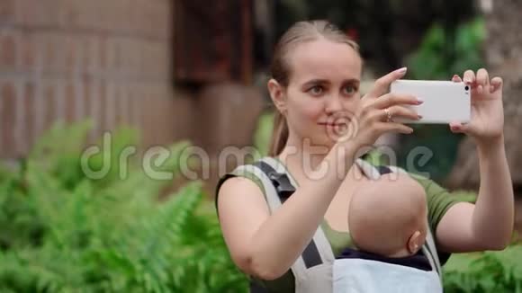 妈妈妈妈带着婴儿带着吊带在岛上旅行用智能手机拍照社交视频的预览图