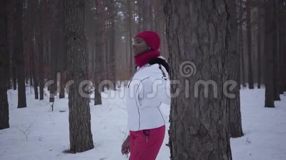 站在冬季森林里的非裔美国女孩她的手放在树上侧着身子漂亮女孩花时间视频的预览图