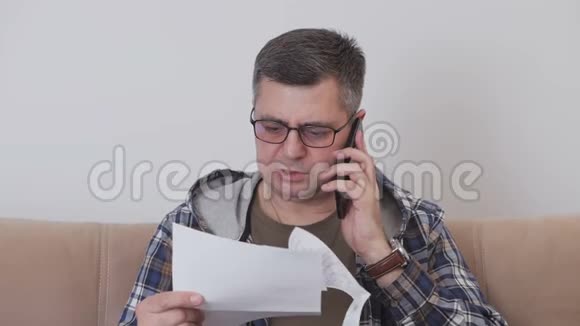 一名中年男子坐在酒店房间的沙发上拿着一份纸质文件在电话中交谈视频的预览图