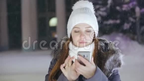 一位女士在圣诞树附近的广场上戴着智能手机在社交网络上分享照片视频的预览图
