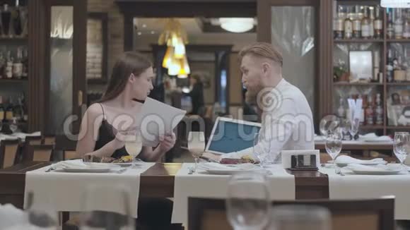 年轻漂亮的女人坐在餐厅的桌子上桌上摆着一张纸上面有一个成熟的蓄着胡须的男人他向她展示了她在餐馆里的信息视频的预览图