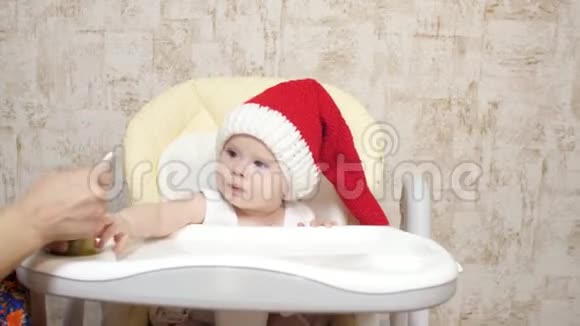 宝贝穿着红色圣诞老人帽子吃土豆泥妈妈给小圣诞老人喂粥戴圣诞帽的孩子视频的预览图