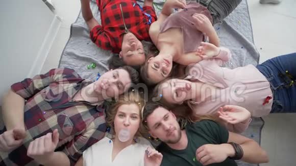 在家庭聚会上快乐的朋友躺在背上一起吹泡泡糖对着镜头微笑视频的预览图