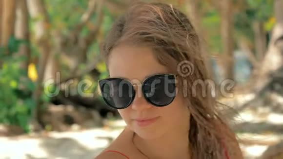 一幅美丽的欧洲年轻女子的特写慢镜头肖像戴着太阳镜头发在热带海滩热带海滩上视频的预览图