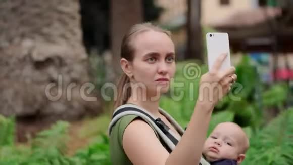 妈妈带着婴儿手里拿着智能手机通过视频与朋友交流视频的预览图