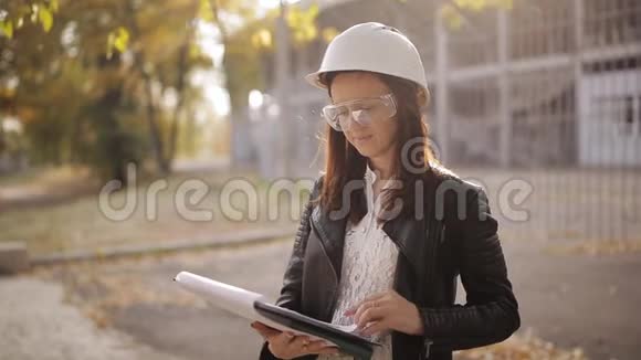 年轻白种人女建筑师站在建筑工地上拿着剪贴板和写作的肖像视频的预览图