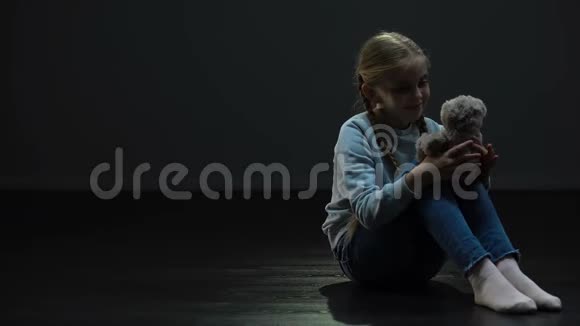 小女孩带着泰迪熊独自坐在黑暗的房间里四处张望孤儿视频的预览图