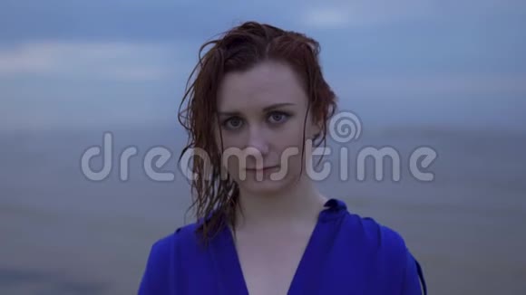 特写一幅年轻红发女子的肖像她穿着一件蓝色连衣裙头发湿漉漉的穆迪冷冷的日落带着生动的洋红色视频的预览图