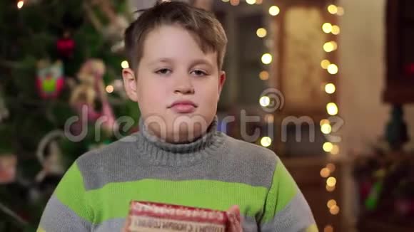 穿着毛衣的少年拿出礼物并微笑在圣诞灯的背景下视频的预览图